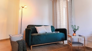 A cozy living room with a teal sofa, a floor lamp, a small table with a plant, and a basket with a blanket.