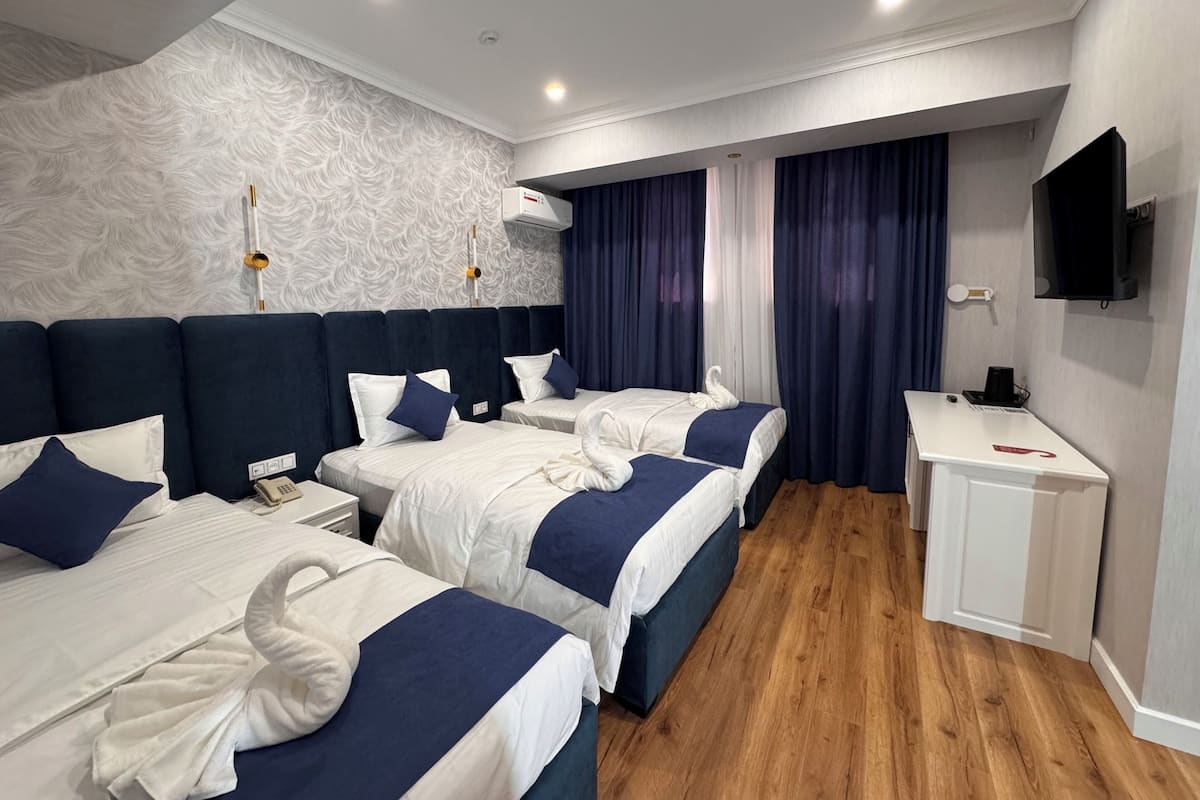 Habitación de hotel con dos camas, un escritorio, un televisor de pantalla plana y un aire acondicionado instalado en la pared.