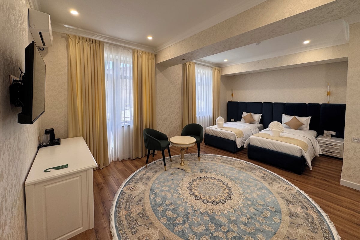 Habitación de hotel con cama, mesitas de noche, escritorio, una silla, alfombra redonda y cortinas.