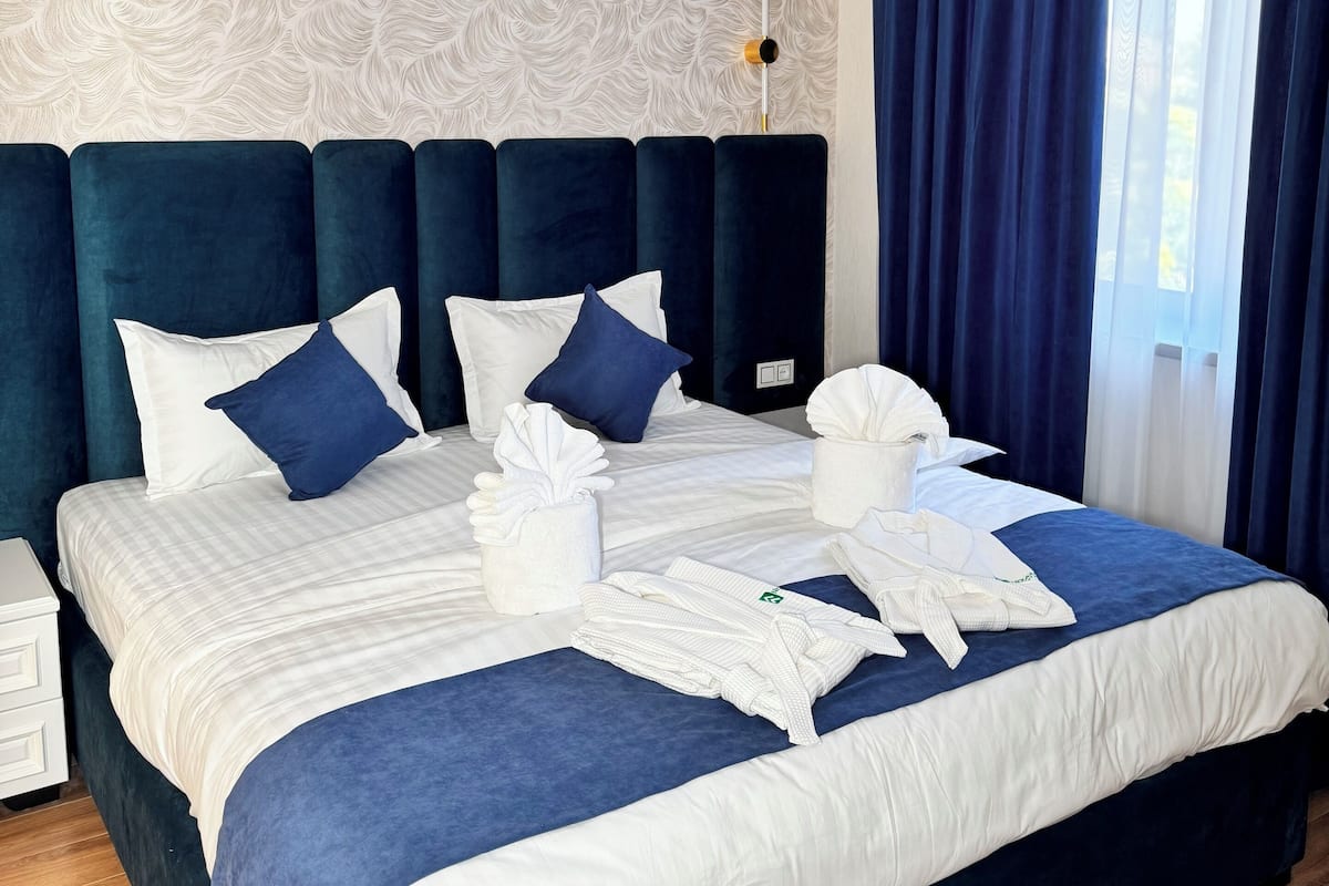 Una cama bien hecha con ropa de cama blanca y azul, un cabecero y una mesita de noche con una lámpara.
