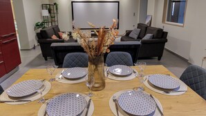 Un comedor con una mesa de madera preparada para seis personas, rodeada de sillas tapizadas en tonos oscuros. Un jarrón con plantas secas está colocado en el centro.