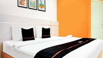 A hotel room with a bed, white bedding, two black pillows, and a black and orange throw. There are three framed artworks on the wall.