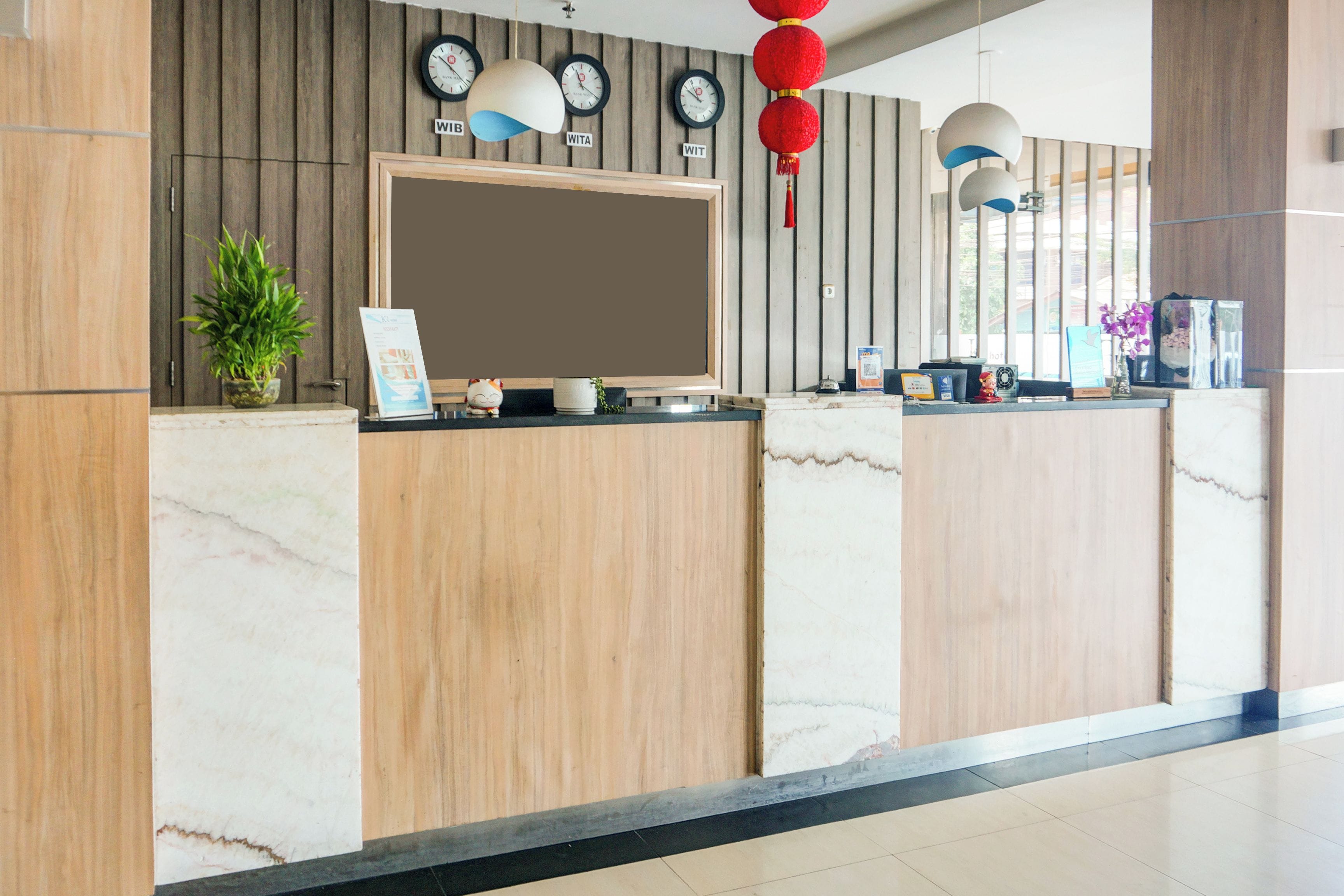 A reception desk with a flat-screen TV, clocks, and a potted plant.