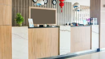 A reception desk with a flat-screen TV, clocks, and a potted plant.