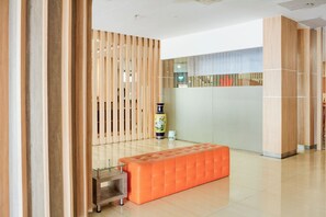 Un lobby moderno con separadores de madera y vidrio, y un área de descanso con un banco acolchado.