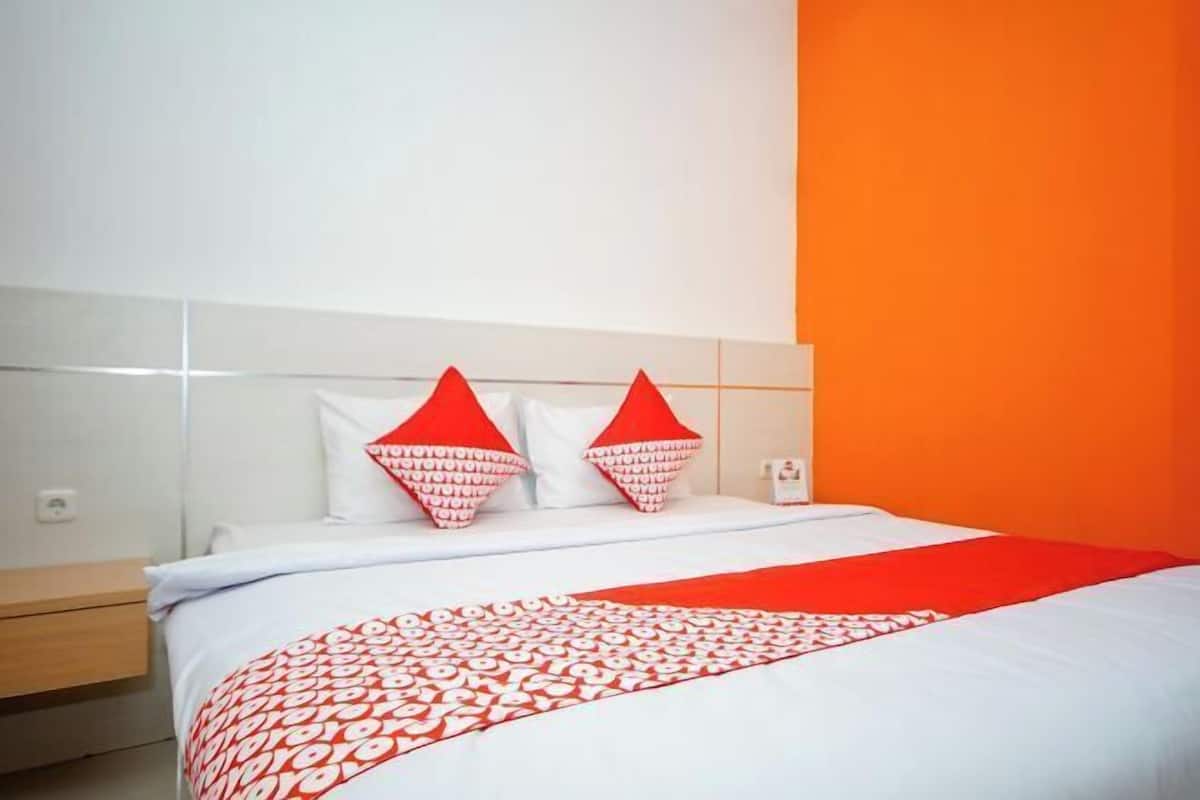 Quarto de hotel com cama, mesa de cabeceira e colcha estampada em vermelho e branco.