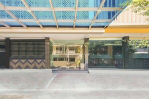 Una entrada de edificio con fachada de vidrio, pared con diseño y estructura de techo metálica.