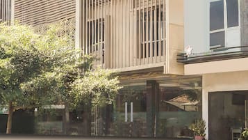 A modern building with a glass facade, vertical wooden slats, and a tree in the foreground.