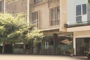 A modern building with a glass facade, vertical wooden slats, and a tree in the foreground. - Townhouse Oak Palembang near Palembang Golf Club formerly KR Hotel (Palembang)