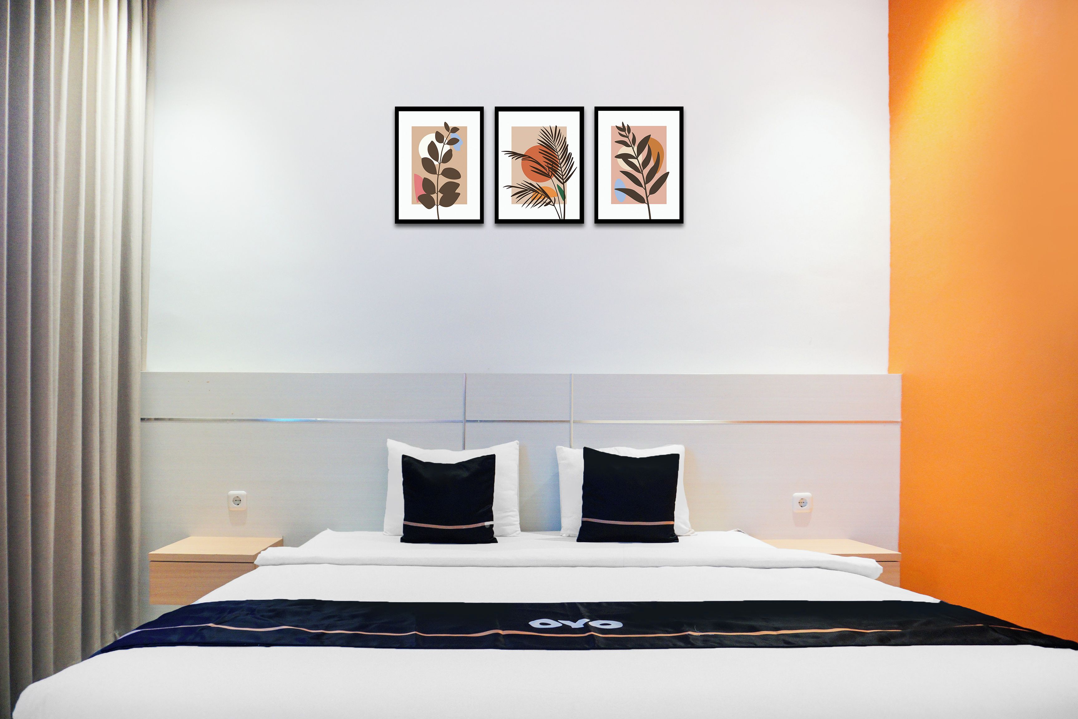 A hotel room with a bed, two bedside tables, a headboard, and three framed artworks on the wall.