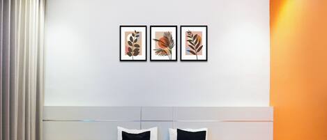 A hotel room with a bed, two bedside tables, a headboard, and three framed artworks on the wall.