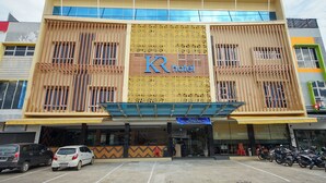 Un hotel con un llamativo letrero 'KR hotel', un estacionamiento con varios coches y una fila de motocicletas estacionadas afuera.
