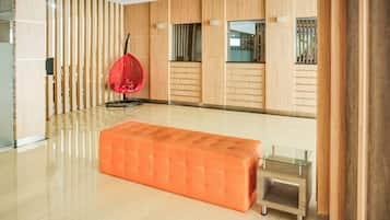 A spacious room with a large orange ottoman, a red hanging chair, and a glass coffee table.