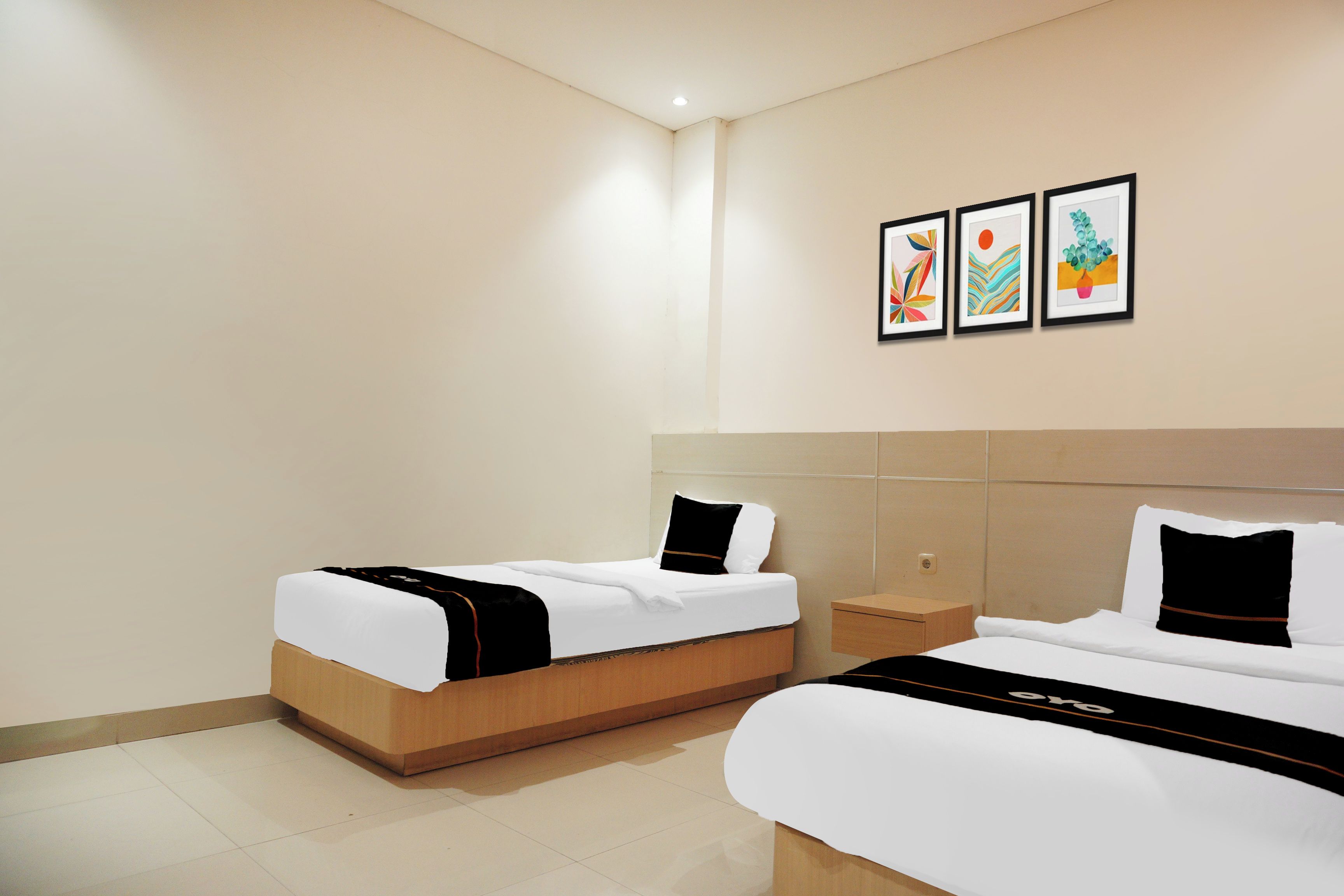 A hotel room with two beds, a small bedside table, and three framed artworks on the wall.