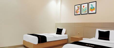 A hotel room with two beds, a small bedside table, and three framed artworks on the wall.