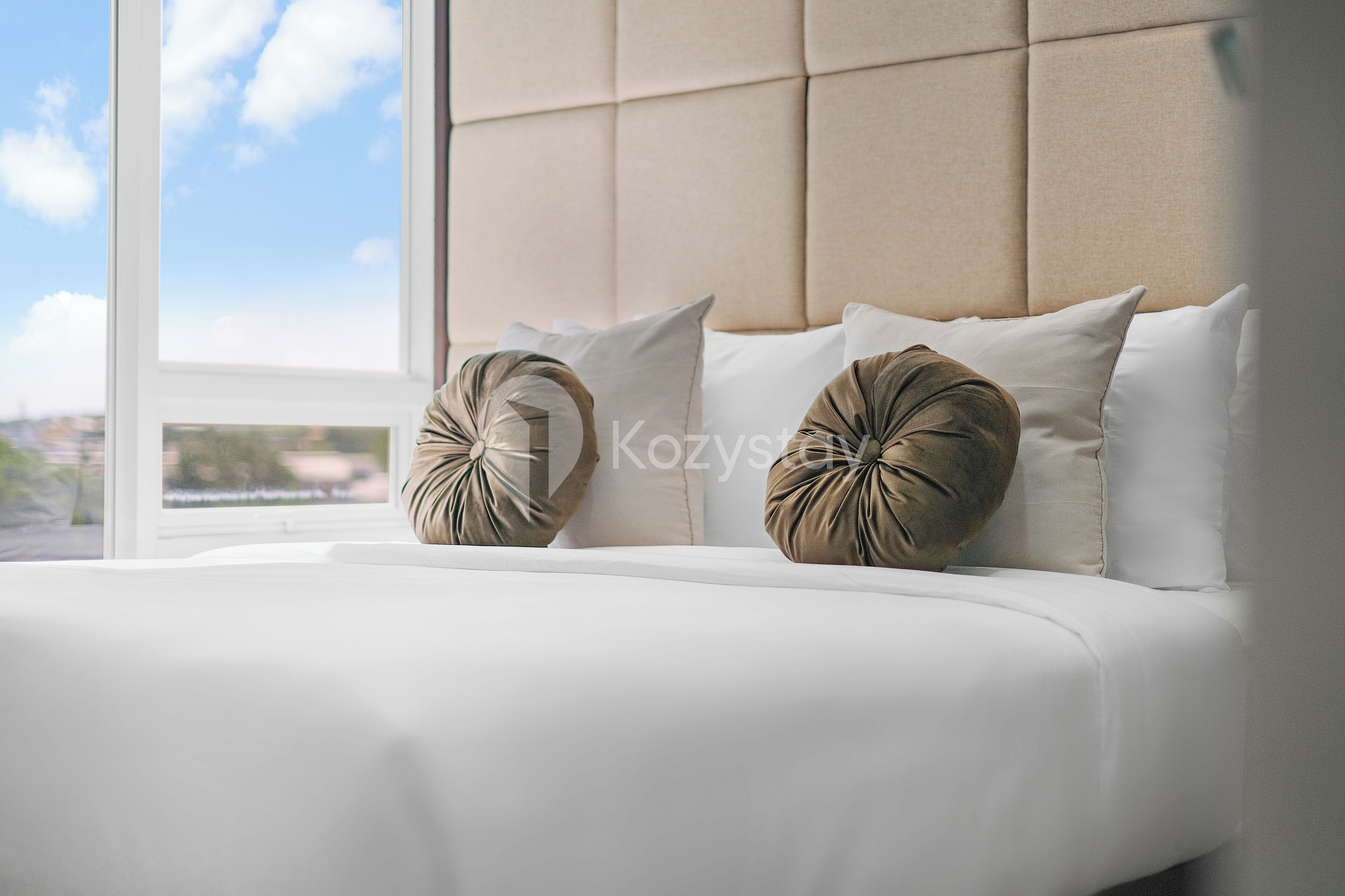A modern hotel room with a large window, a tufted headboard, and two decorative pillows.