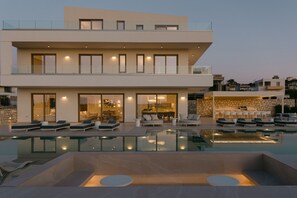 Una casa moderna de dos pisos con piscina, mobiliario exterior y un interior bien iluminado.