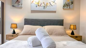 Habitación de hotel con cama, dos lámparas de noche, un cuadro grande de pájaros en la pared y una ventana a la izquierda.