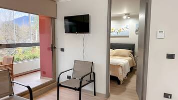 A modern bedroom with a bed, a chair, a TV, and a window with a view of trees.
