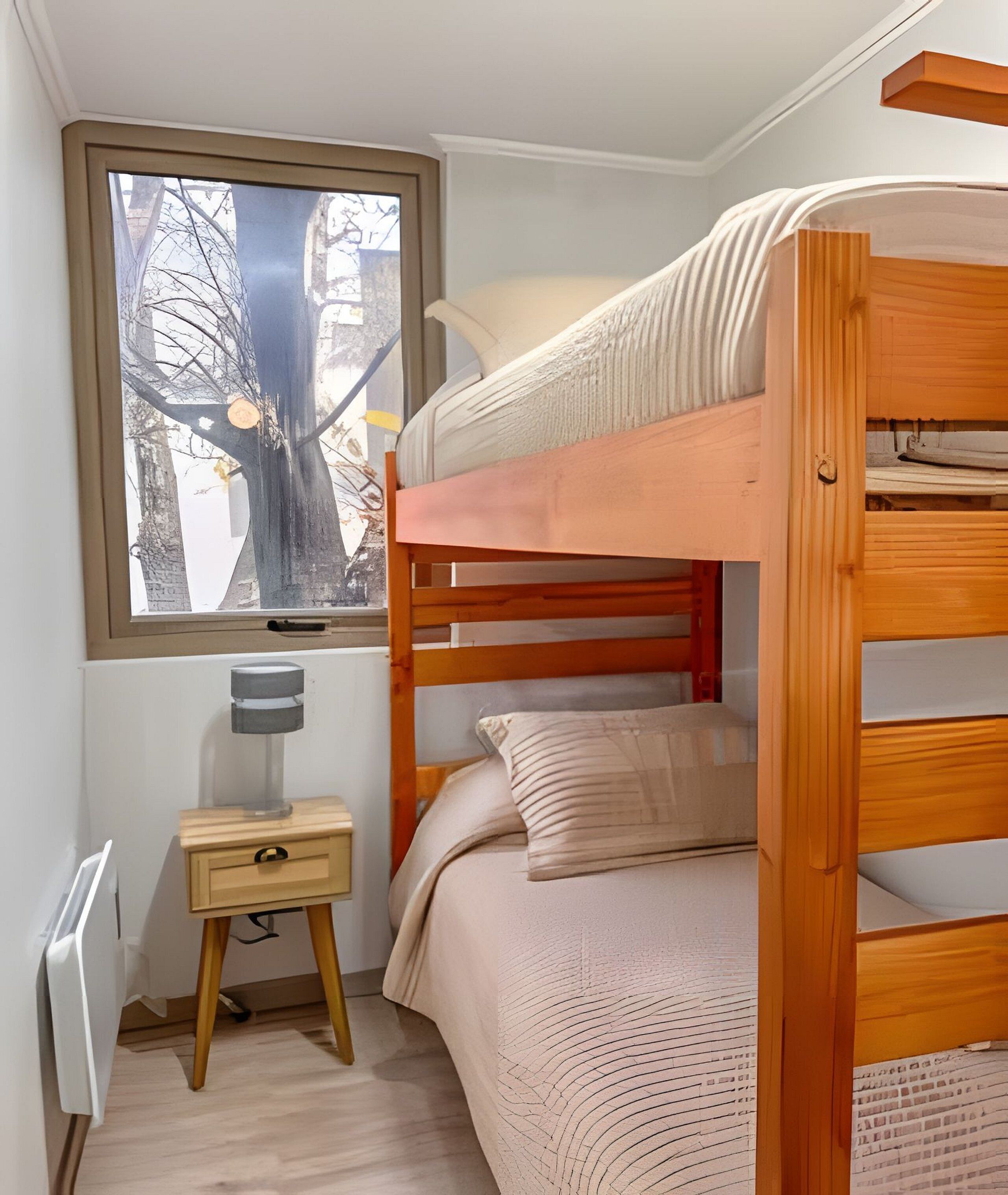 A bunk bed room with a window, a bedside table, and a radiator.