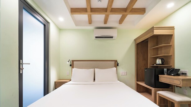A hotel room with a bed, a desk, a chair, a wardrobe, and an air conditioning unit. - Nicecy Hotel - Truong Quyen (Ho Chi Minh City)