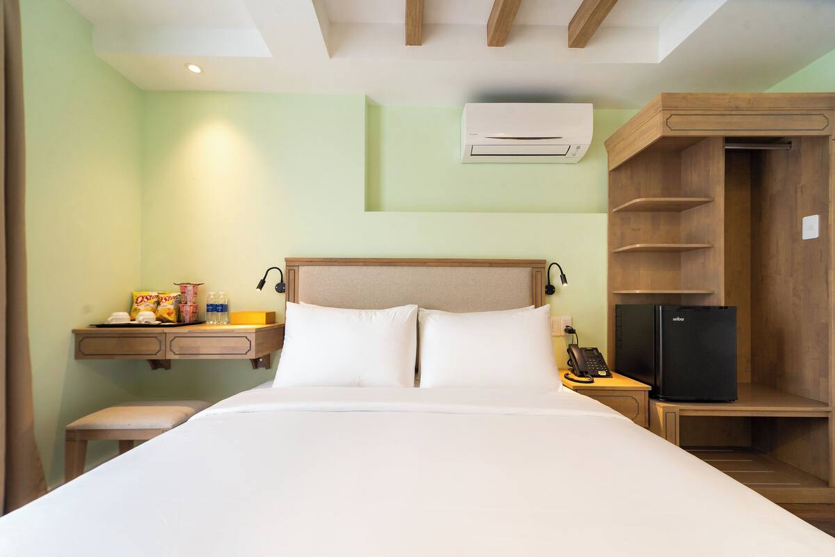 A hotel room with a bed, a desk with snacks, a refrigerator, and a built-in wardrobe.