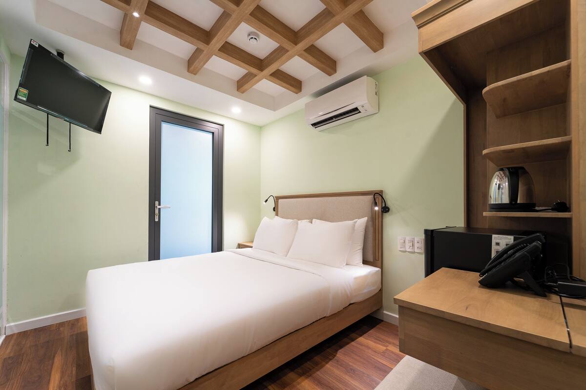 A bedroom with a bed, a desk, a TV, and an air conditioner.