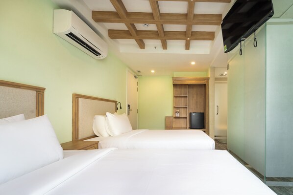 A hotel room with two beds, a TV, a wardrobe, and a small seating area.