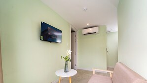 A room with a TV mounted on the wall, a small round table with a vase, a sofa, and an air conditioning unit. - Nicecy Hotel - Truong Quyen (Ho Chi Minh City)
