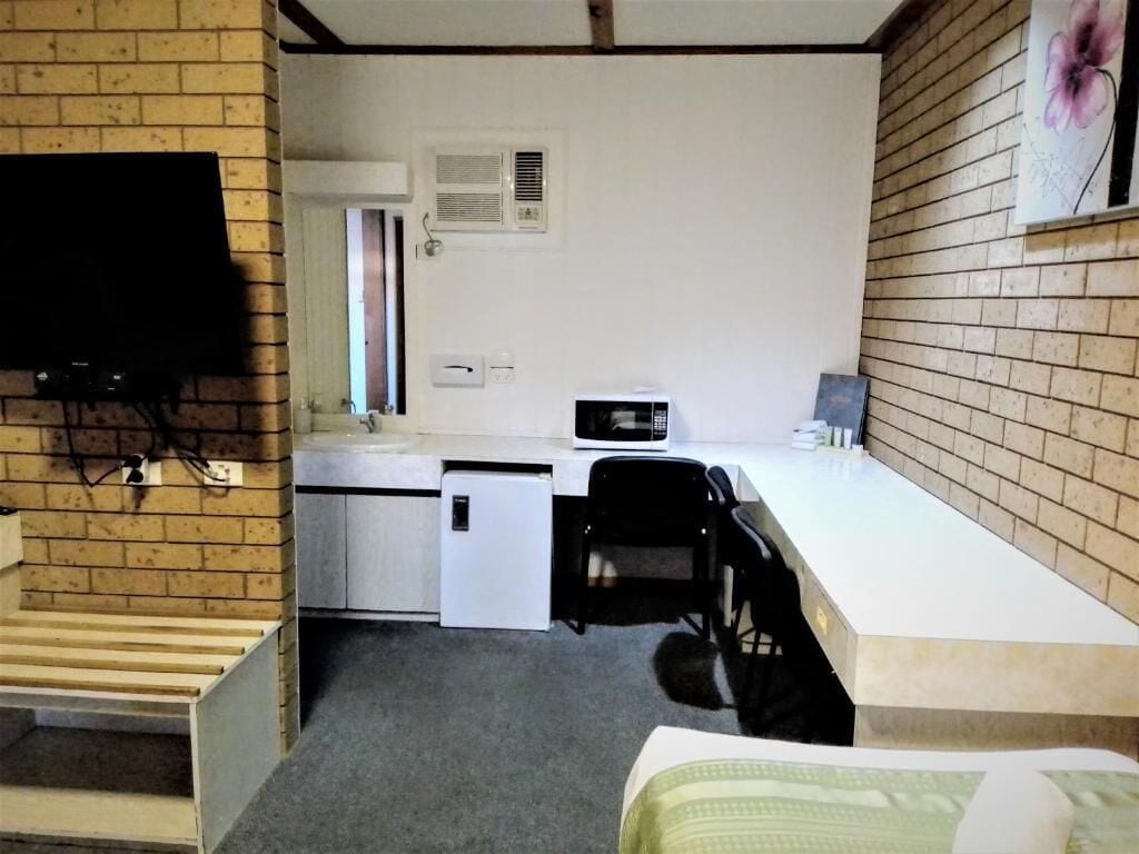 A compact room with a kitchenette, a bed, a desk, and a TV mounted on the wall.