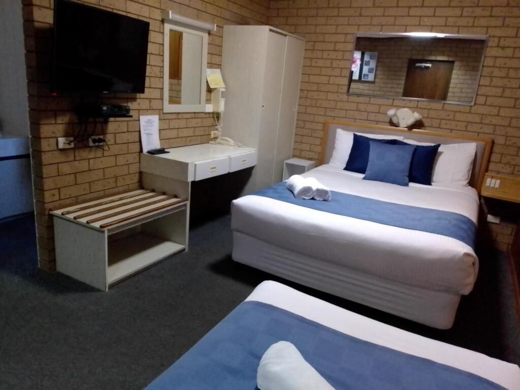A hotel room with a bed, a desk, a chair, a TV, and a wardrobe.