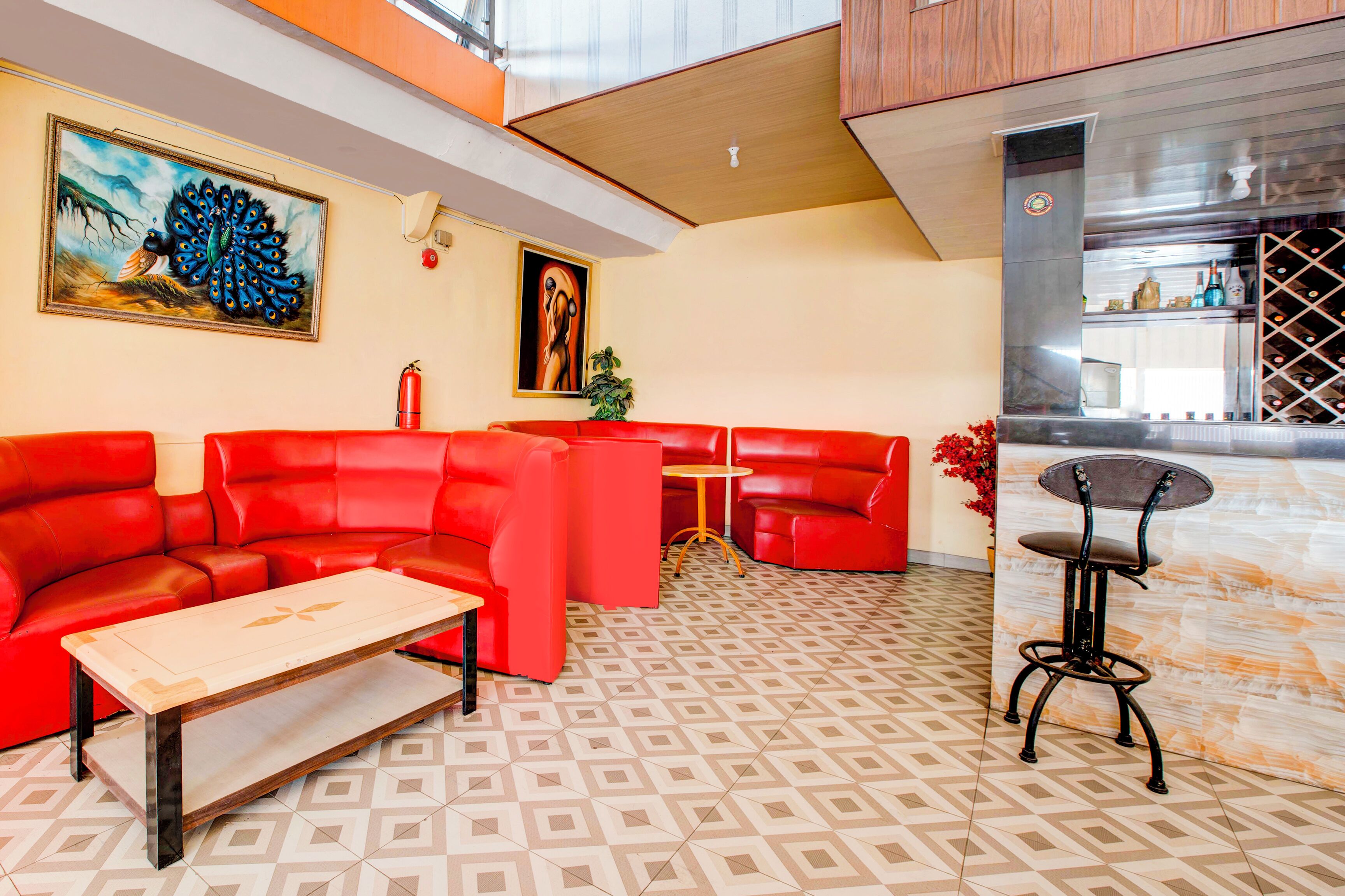 Um lobby moderno de hotel com sofás de couro vermelho, uma mesa de centro de madeira, área de bar com adega e obras de arte nas paredes.