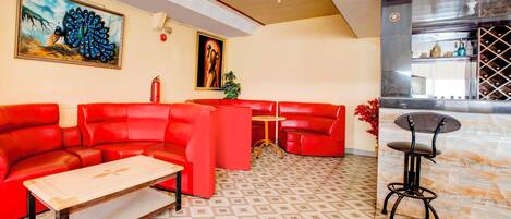 Um lobby moderno de hotel com sofás de couro vermelho, uma mesa de centro de madeira, área de bar com adega e obras de arte nas paredes.