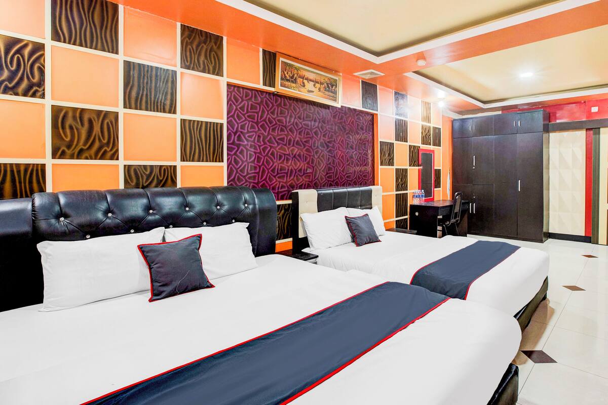 A hotel room with two beds, a large headboard, and a patterned wall.