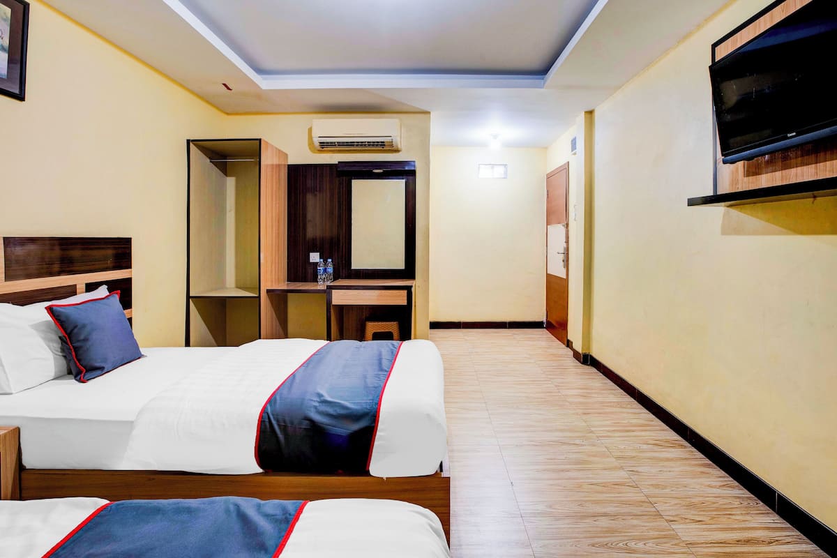 A hotel room with two beds, a desk, a mirror, and a TV mounted on the wall.