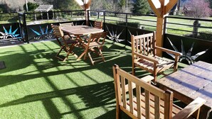 An outdoor patio with a wooden table and chairs, surrounded by a metal fence and a view of a mountainous landscape. - LE POTZ" 1 double room (Tour-de-Faure)