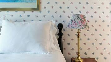 A neatly made bed with white linens, a floral-patterned lamp on a wooden nightstand, and a wall with a floral wallpaper pattern.