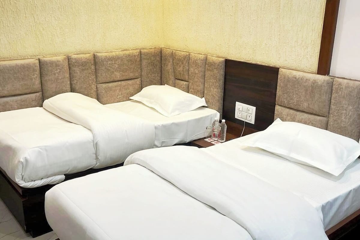 Habitación de hotel con dos camas individuales, cada una con ropa blanca y cabecero. Hay una mesita de noche con una lámpara y una botella de agua.