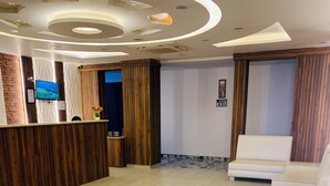 A modern reception area with a wooden reception desk, a flat-screen TV, and a seating area with white sofas. - Hotel jageshwari inn (Gwalior)