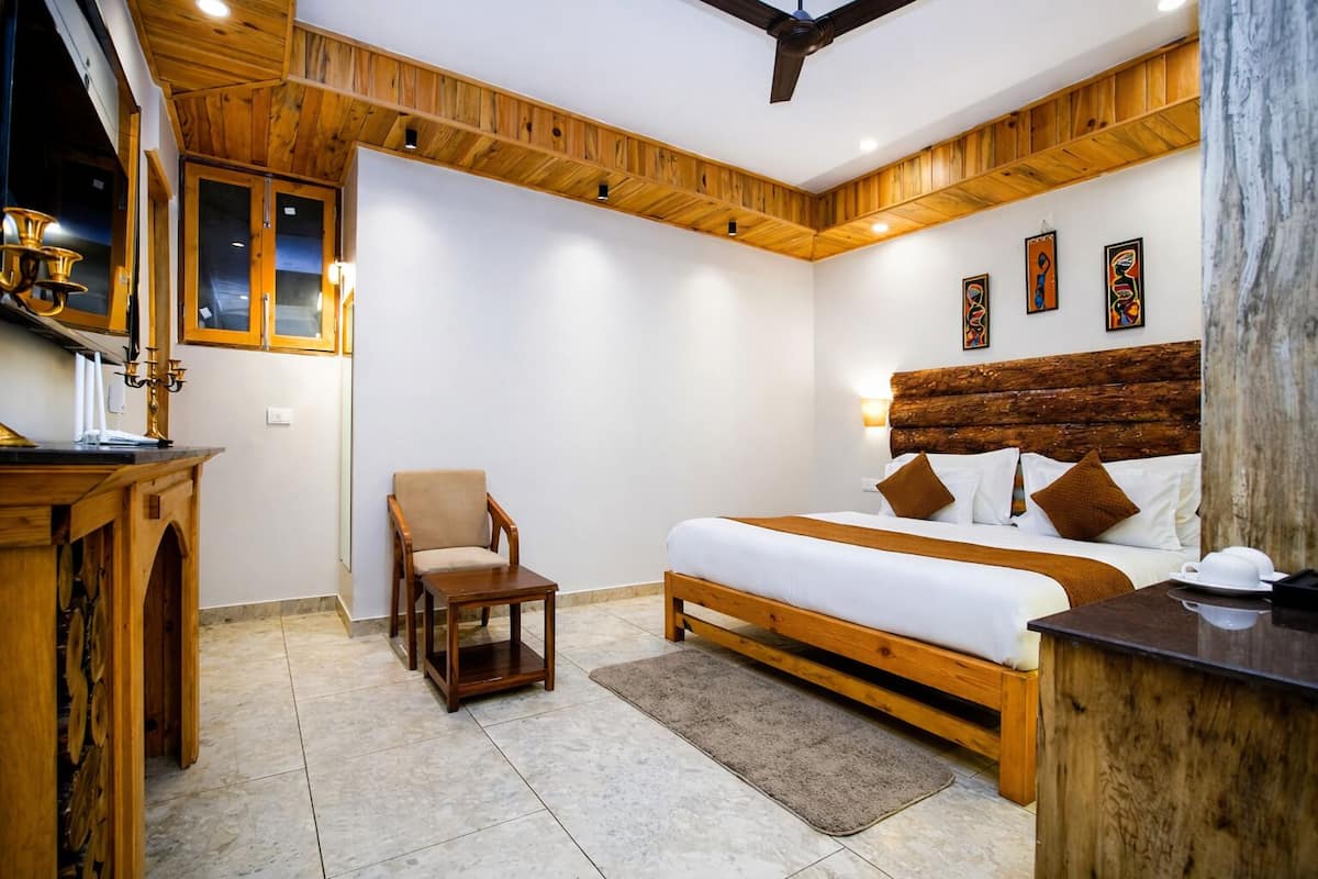 A hotel room with a wooden ceiling, a bed with a wooden headboard, a chair, a desk, and artwork on the wall.