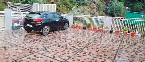A black car parked on a tiled patio with a white fence and potted plants.