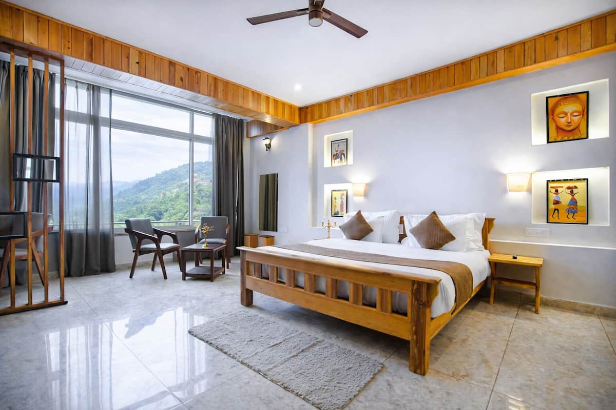 A spacious bedroom with a large bed, wooden headboard, a desk, and a chair. There are two wall-mounted lights and a ceiling fan.
