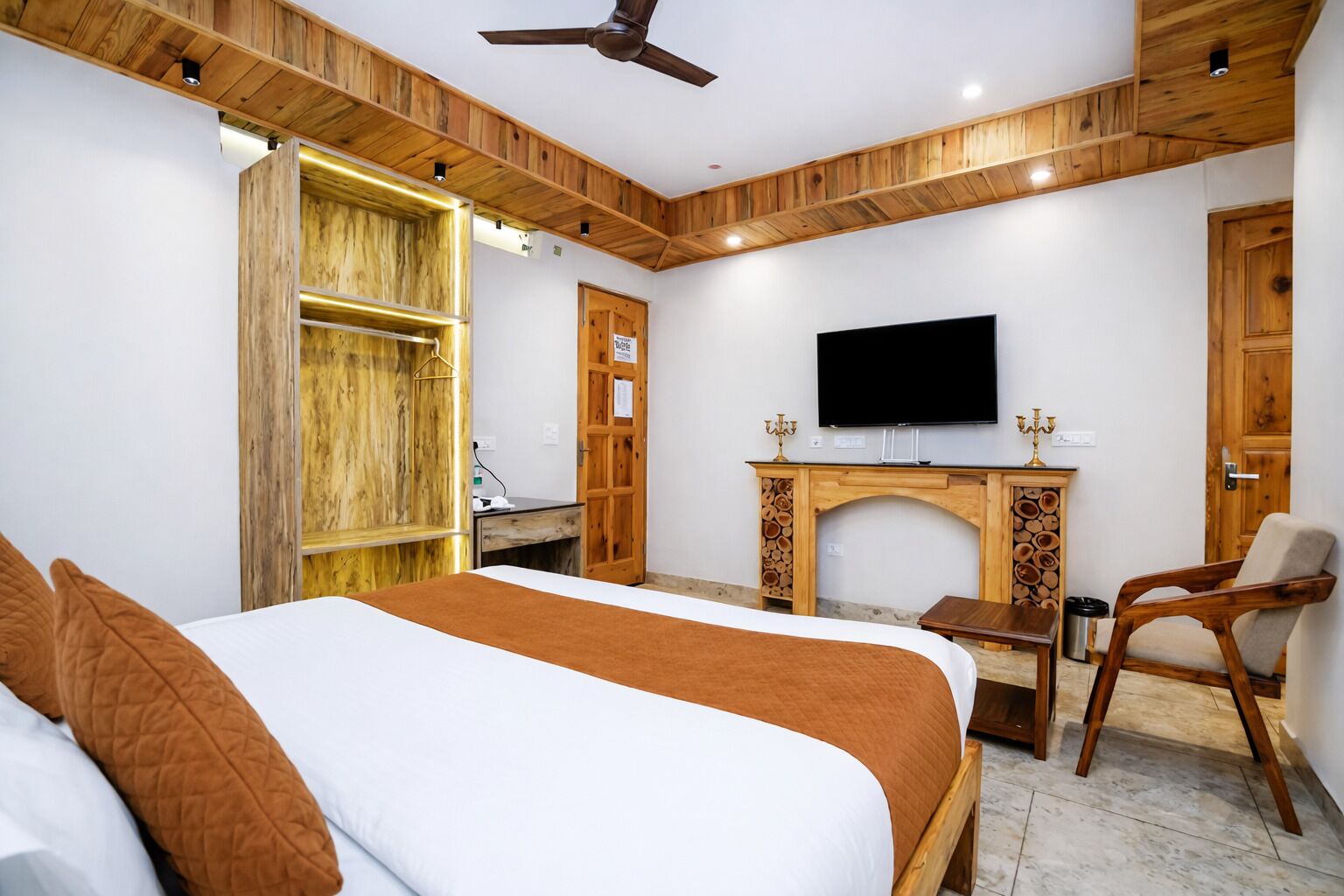 A bedroom with a bed, a TV, a wooden cabinet, and a fireplace.