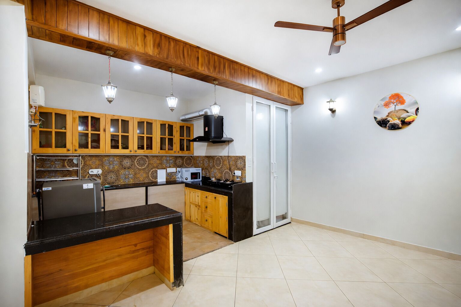 Una cocina con armarios de madera, encimera negra, microondas y ventilador de techo.
