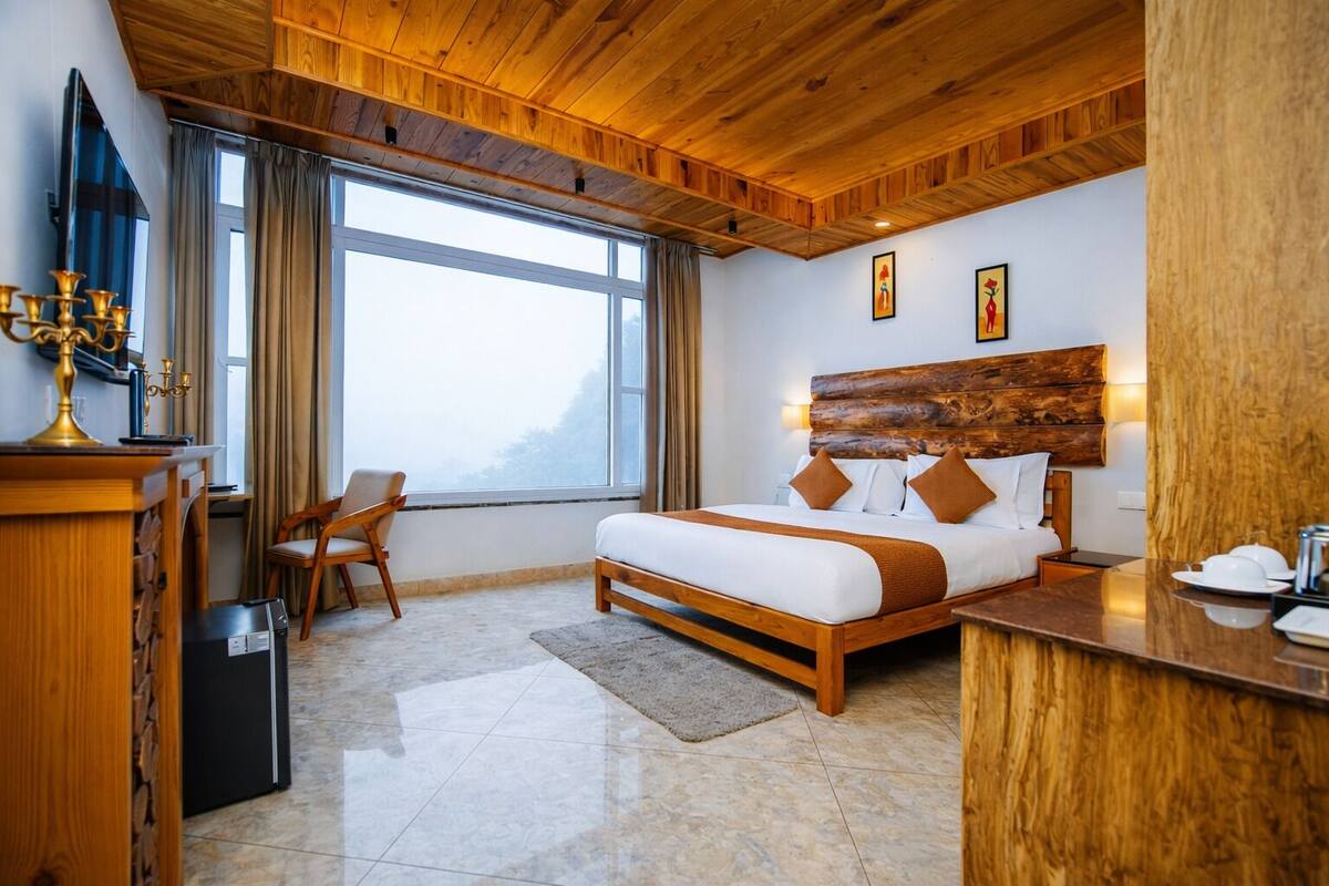 A hotel room with a wooden ceiling, a large bed with white and brown bedding, a desk with a computer, and a chair.