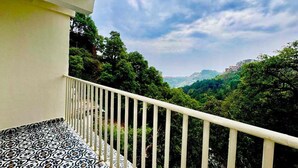 A balcony with a patterned floor, overlooking a lush green landscape and distant buildings.