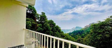 A balcony with a patterned floor, overlooking a lush green landscape and distant buildings.