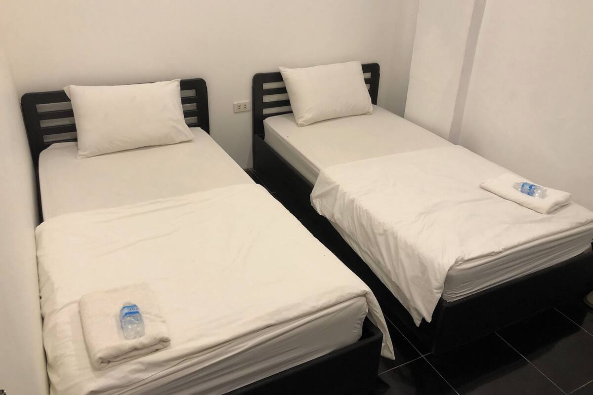 Two single beds with white linens and pillows, a water bottle on the left bed, and a towel on the right bed.
