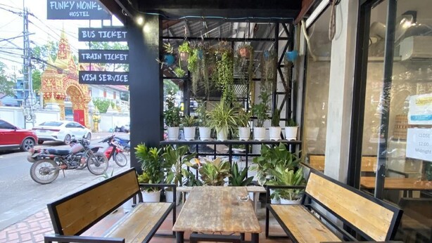 An outdoor seating area with benches and tables, surrounded by potted plants. - Funkymonkey Cafe&hostel (Vientiane)