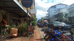 A street with a brick sidewalk, parked motorcycles, and a building with a sign reading "Pimenton". - Funkymonkey Cafe&hostel (Vientiane)